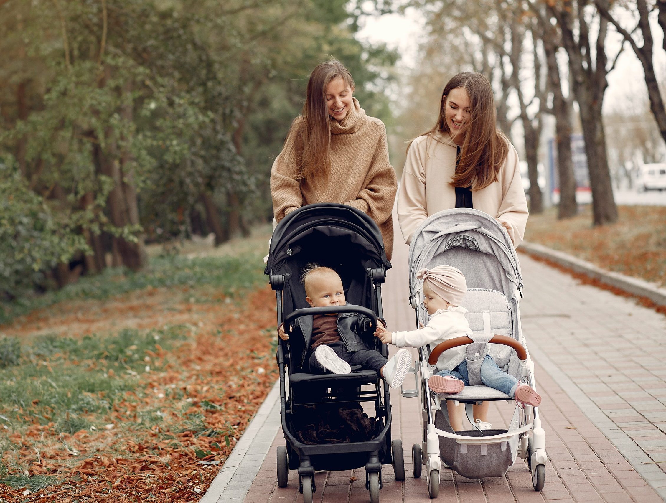 Two young mothers walking in a autumn park with carriages